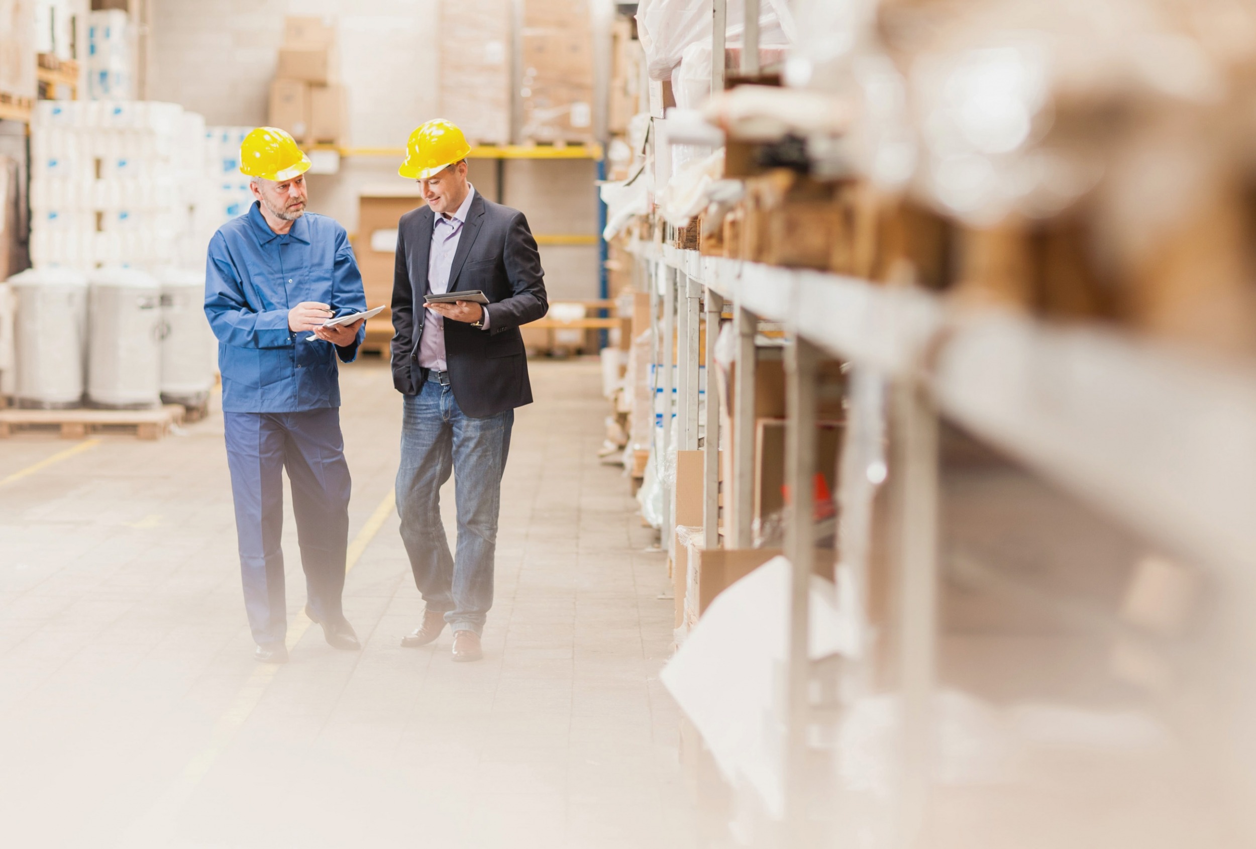 Men wearing hardhats and reading tablets in warehouse