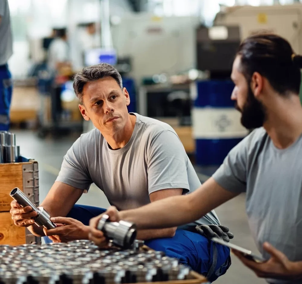 Two men inspecting parts in manufacturing plant, while leveraging a QMS for manufacturing/production